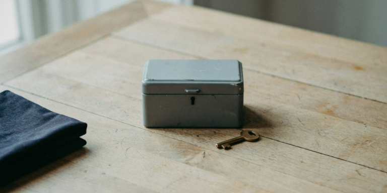 A small grey metal cash box with a brass key beside it on an oak table