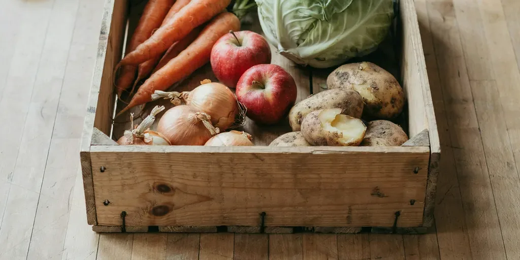 Long-keeping produce on a pale oak table: carrots, cabbage, onions, potatoes and apples in a wooden crate